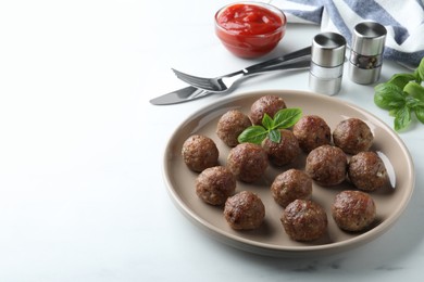 Photo of Tasty cooked meatballs with basil on white table. Space for text