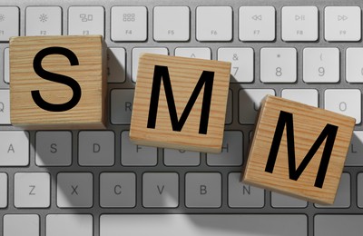 Photo of Wooden cubes with letters SMM on computer keyboard, flat lay