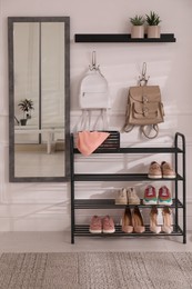 Photo of Black shelving unit with shoes and different accessories near white wall in hall. Storage idea