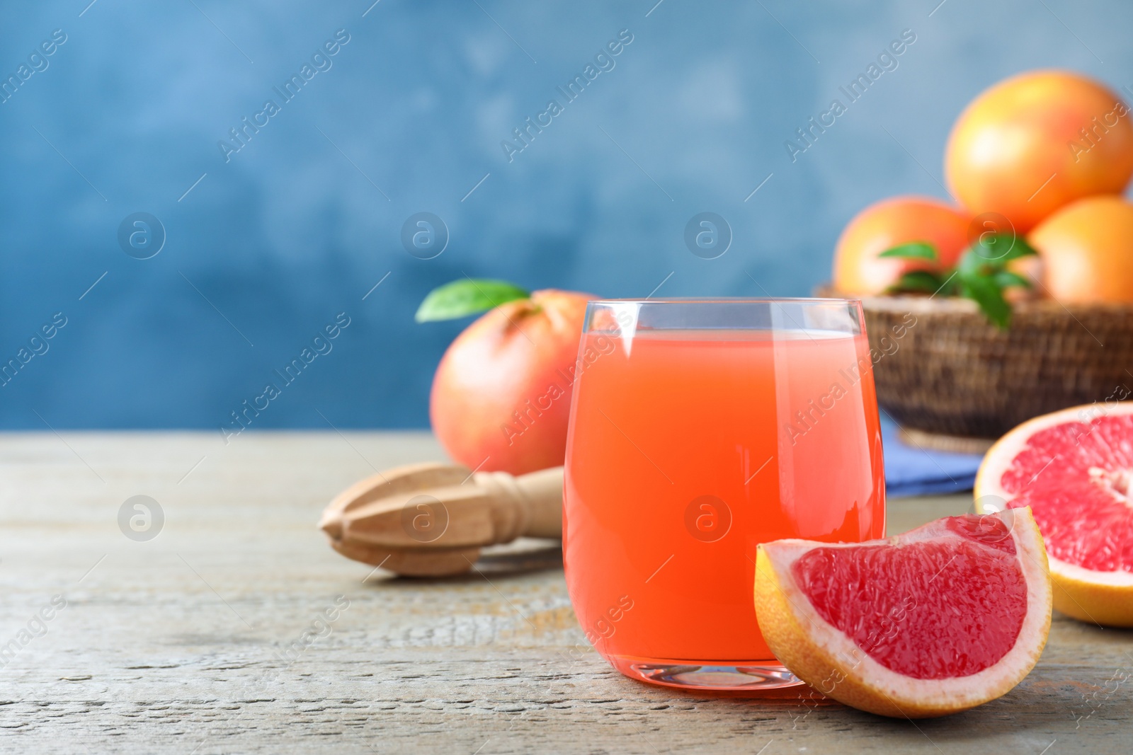 Photo of Tasty freshly made grapefruit juice and fruit on wooden table. Space for text