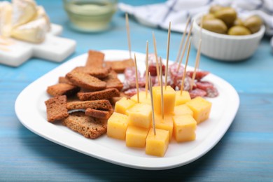 Photo of Toothpick appetizers. Pieces of sausage, cheese and croutons on light blue wooden table, closeup