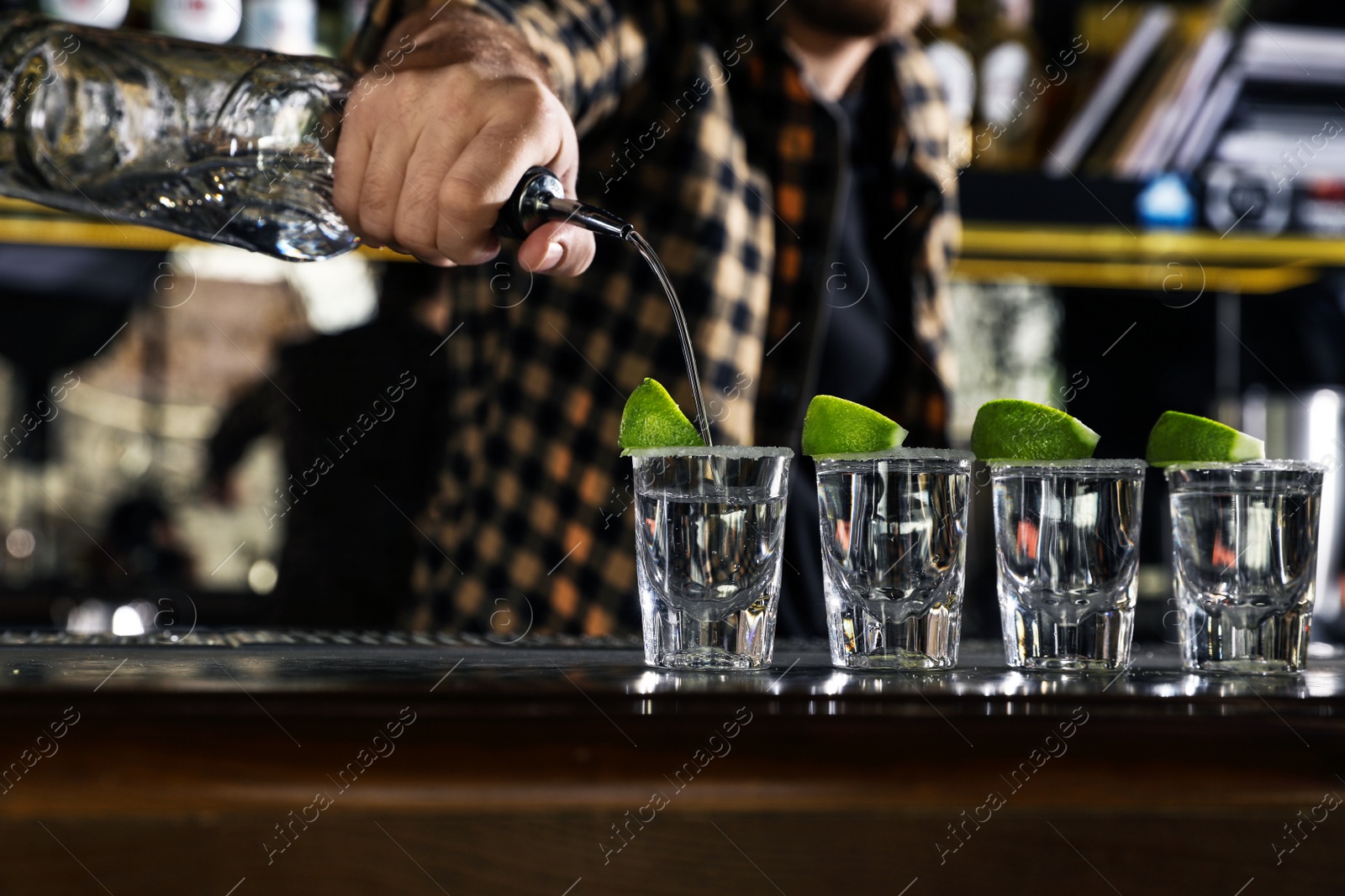 Photo of Bartender pouring Mexican Tequila into shot glasses at bar counter, closeup