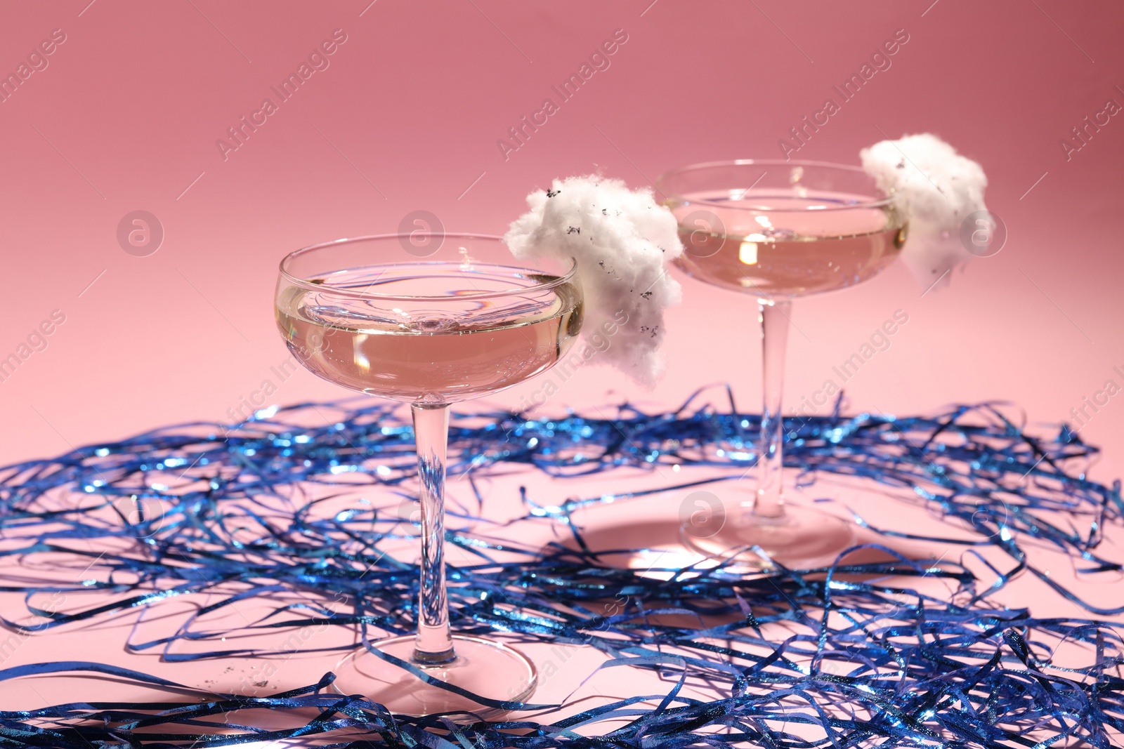 Photo of Tasty cocktails in glasses decorated with cotton candy and blue shiny streamers on pink background