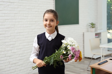 Photo of Happy schoolgirl with bouquet in classroom. Teacher's day