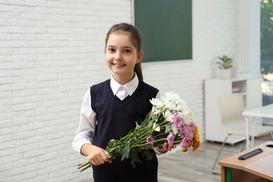 Happy schoolgirl with bouquet in classroom. Teacher's day