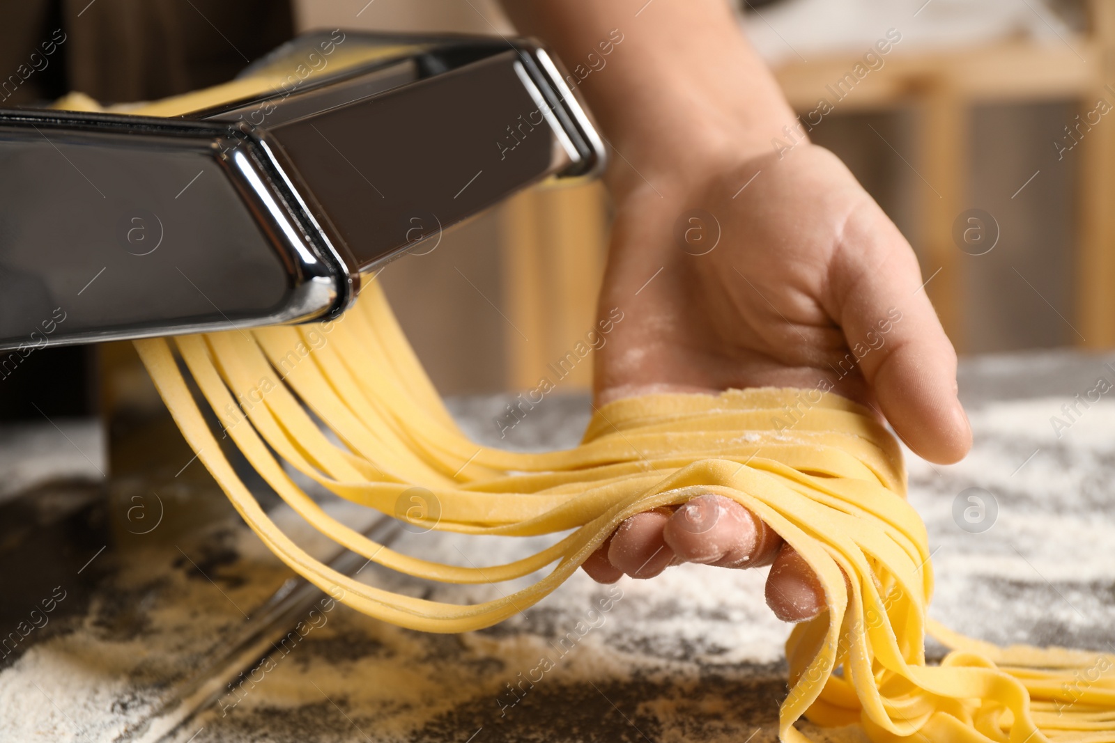 Photo of Woman preparing noodles with pasta maker machine at table indoors, closeup