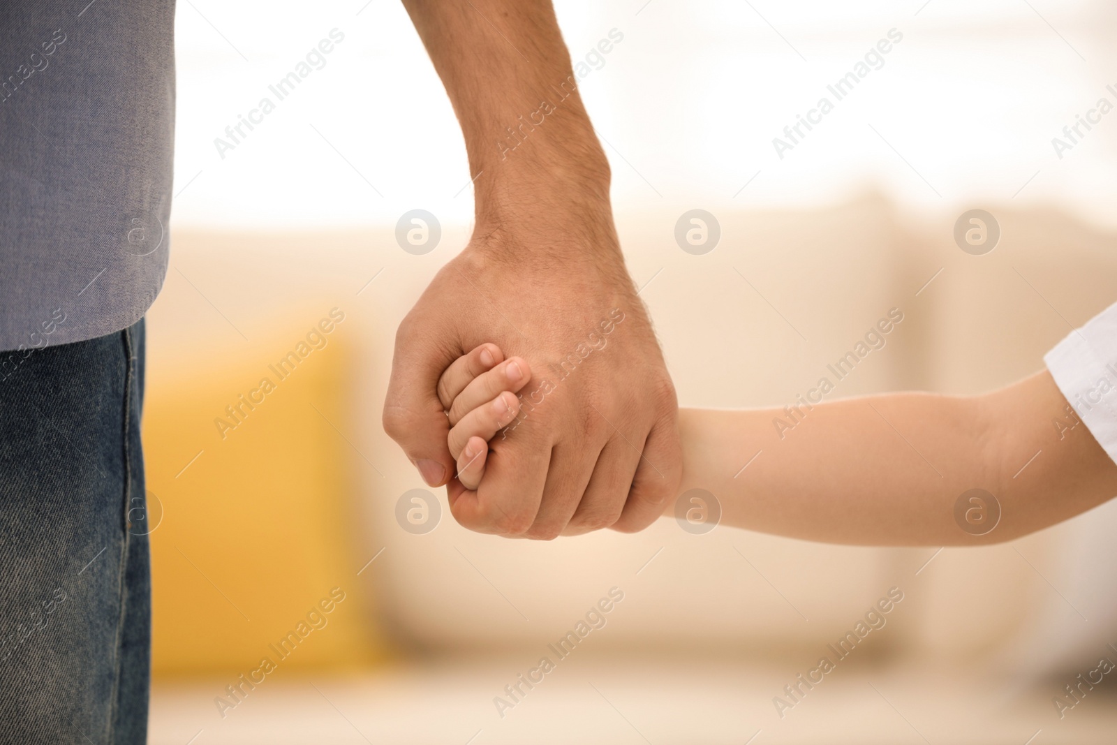 Photo of Father holding hands with his child indoors, closeup. Happy family