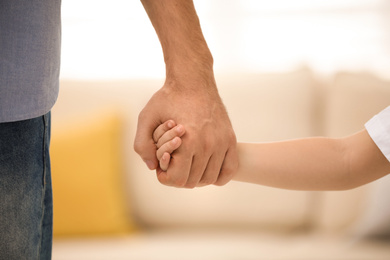 Photo of Father holding hands with his child indoors, closeup. Happy family