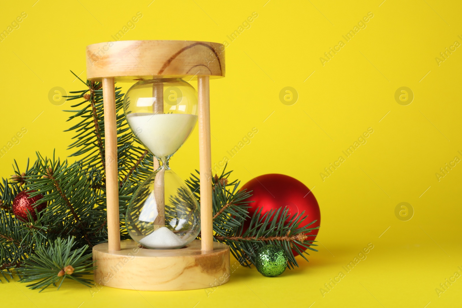 Photo of Hourglass and fir tree with decor on yellow background, space for text. Christmas countdown