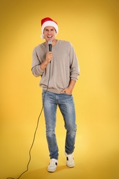 Photo of Happy man in Santa Claus hat singing with microphone on yellow background. Christmas music