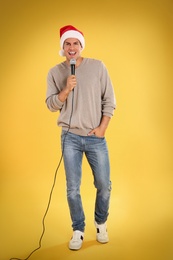 Happy man in Santa Claus hat singing with microphone on yellow background. Christmas music