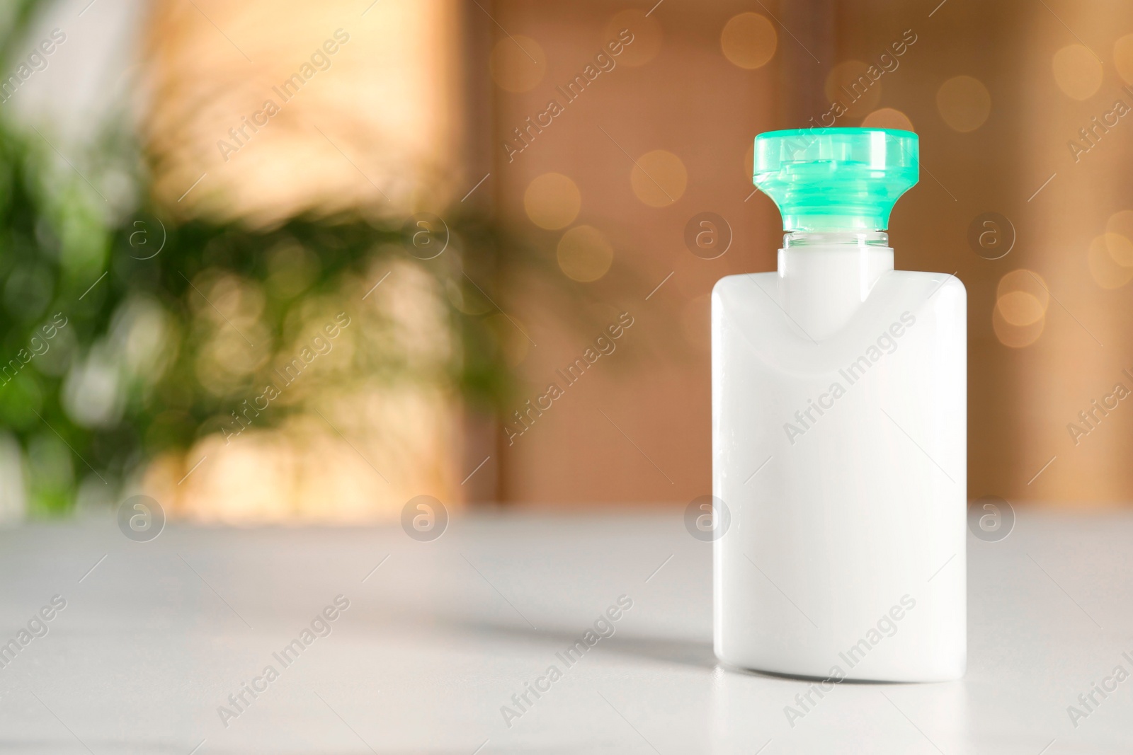 Photo of Mini bottle of cosmetic product on white table against blurred background. Space for text