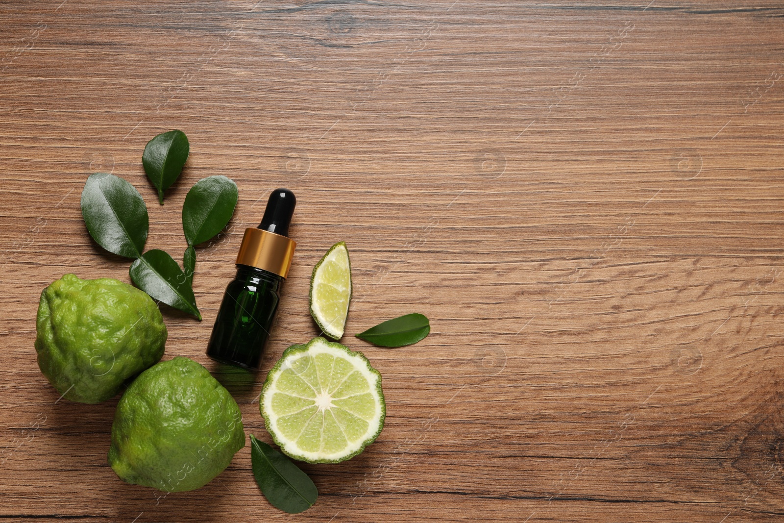 Photo of Glass bottle of bergamot essential oil and fresh fruits on wooden table, flat lay. Space for text