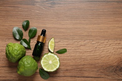 Photo of Glass bottle of bergamot essential oil and fresh fruits on wooden table, flat lay. Space for text