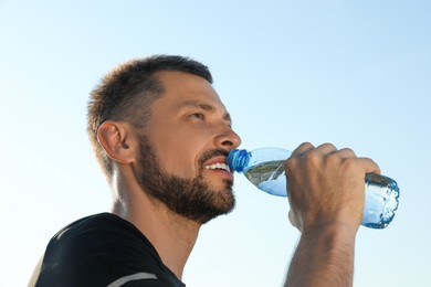 Photo of Happy man drinking water against blue sky on hot summer day. Refreshing drink