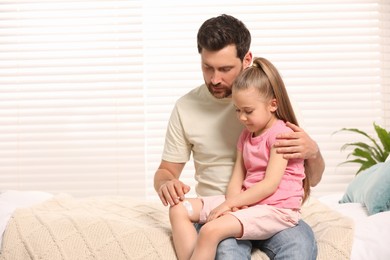 Photo of Father applying ointment onto his daughter's leg on bed indoors