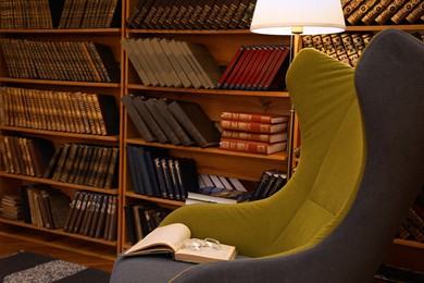 Photo of Comfortable armchair with book and glasses in cozy home library