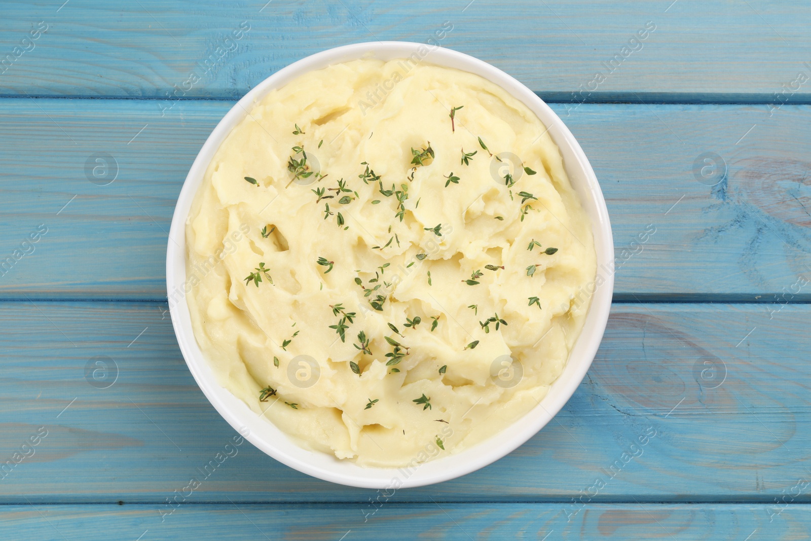 Photo of Bowl of tasty mashed potato with rosemary on light blue wooden table, top view