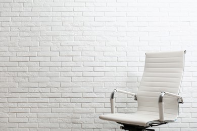 Photo of Comfortable office chair near white brick wall. Space for text