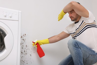 Man in rubber gloves using mold remover on wall in bathroom