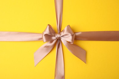 Photo of Beige satin ribbon with bow on yellow background, top view