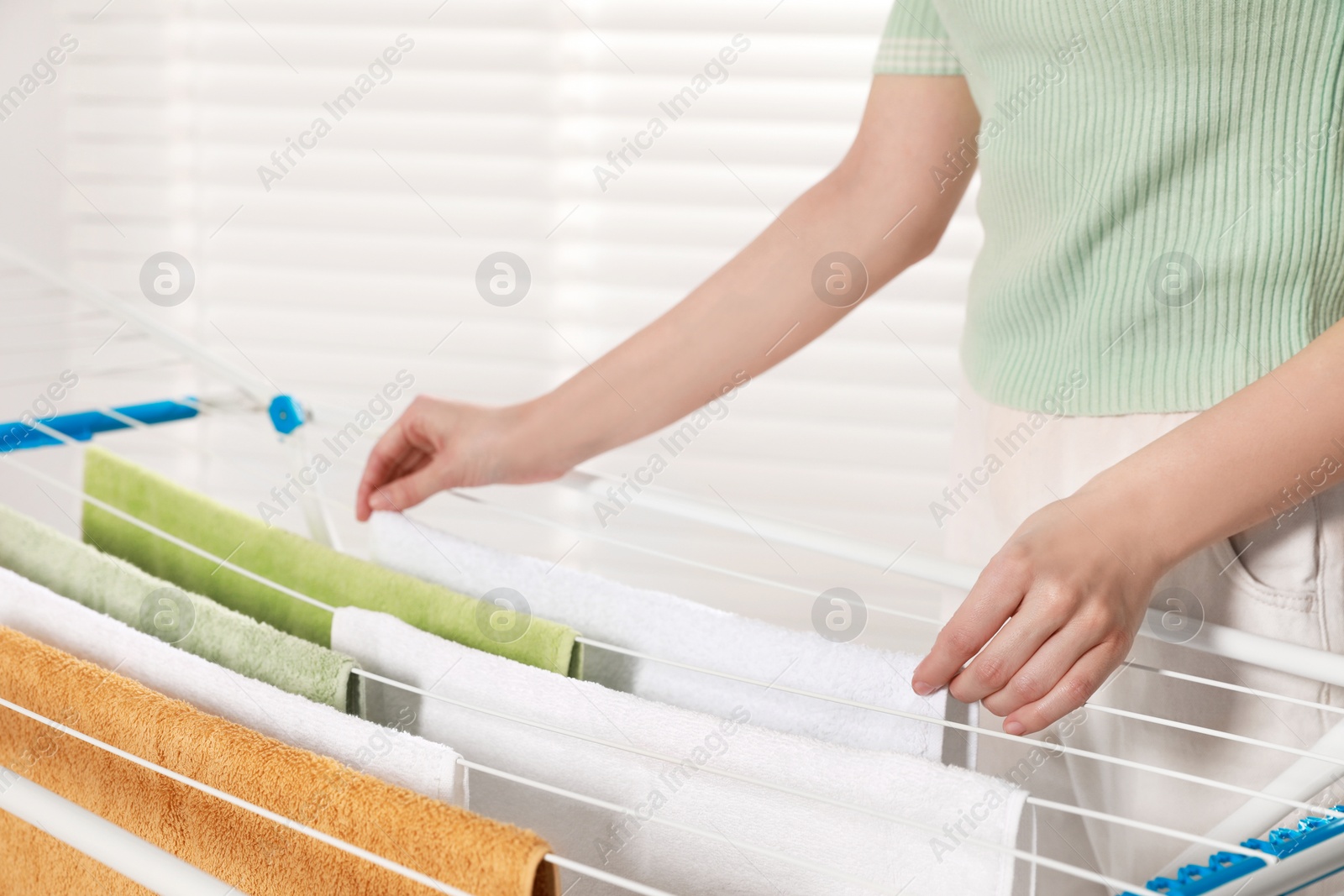 Photo of Woman hanging clean terry towels on drying rack indoors, closeup