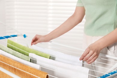 Woman hanging clean terry towels on drying rack indoors, closeup