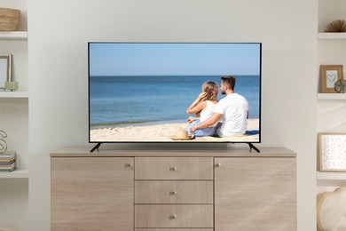 Modern TV set on wooden stand in room. Scene of romantic movie on screen
