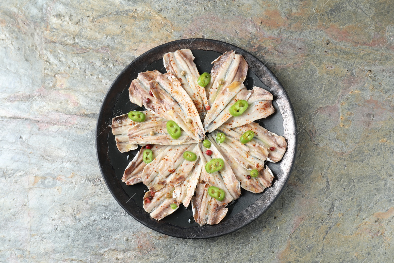 Photo of Tasty pickled anchovies with spices on textured table, top view