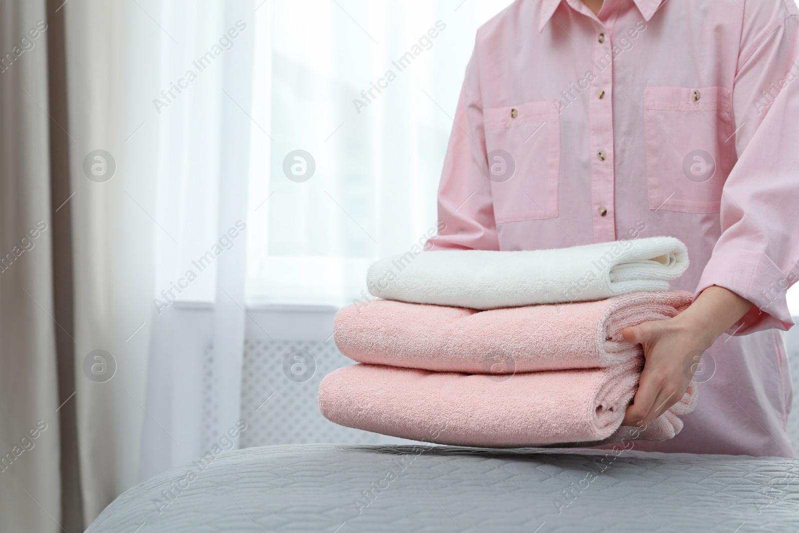 Photo of Woman putting stack of clean towels on bed. Space for text