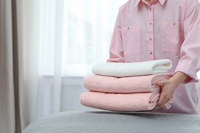 Woman putting stack of clean towels on bed. Space for text