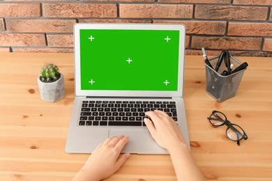 Image of Young woman using laptop at wooden desk, closeup. Device display with chroma key