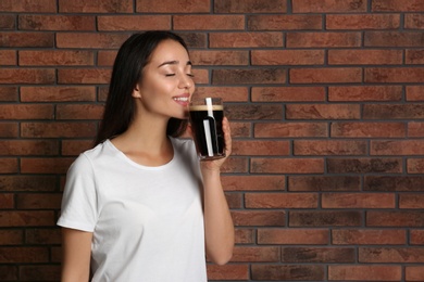 Photo of Beautiful woman with cold kvass near brick wall. Traditional Russian summer drink