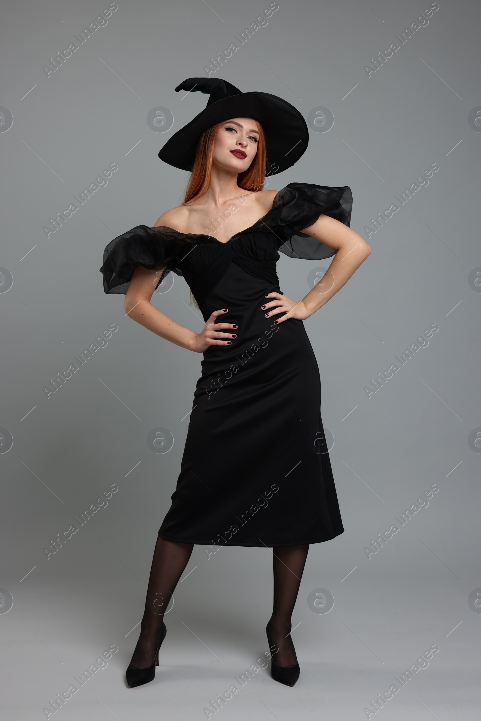Photo of Young woman in scary witch costume posing on light grey background. Halloween celebration