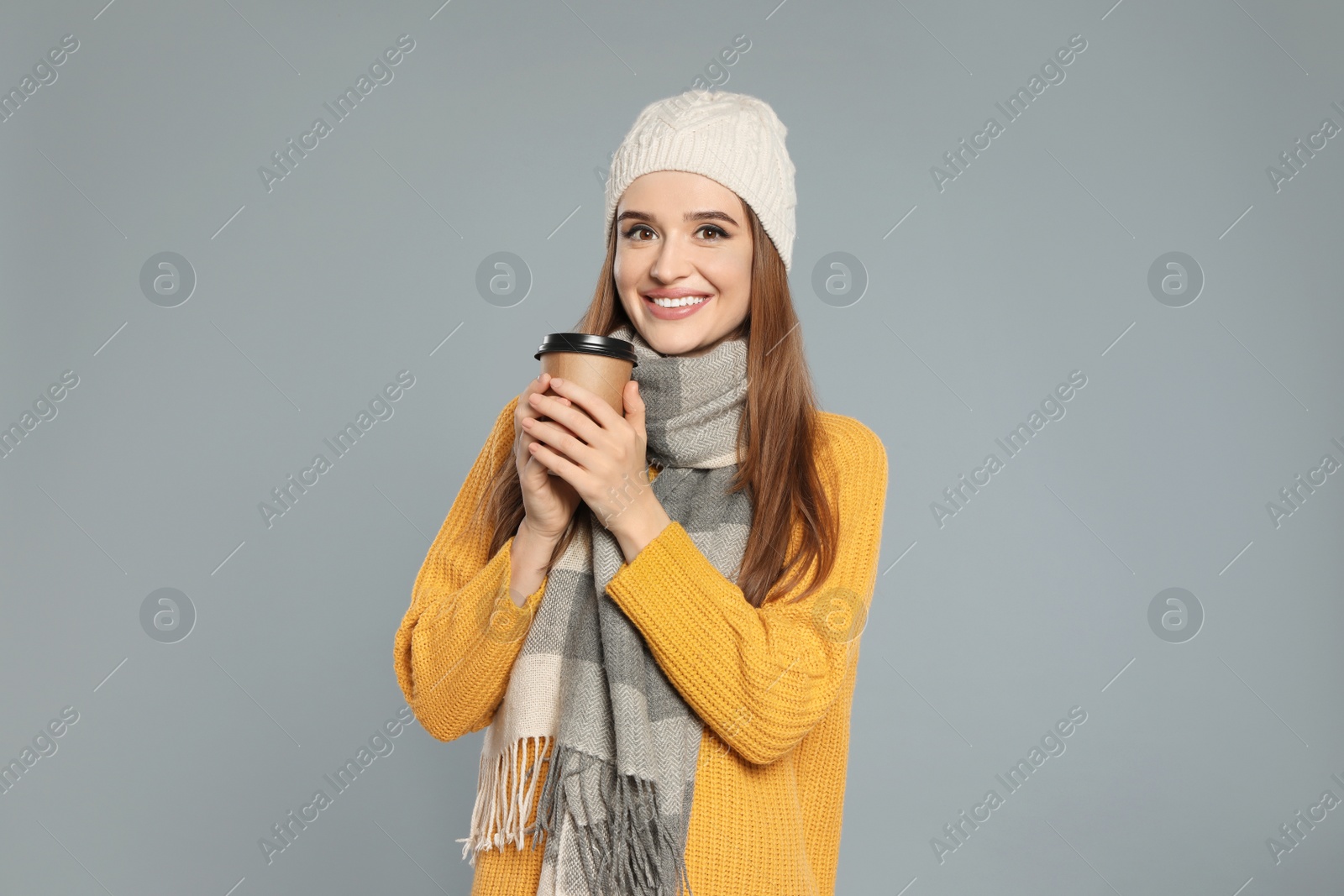 Photo of Happy young woman in warm clothes with drink on grey background. Winter season