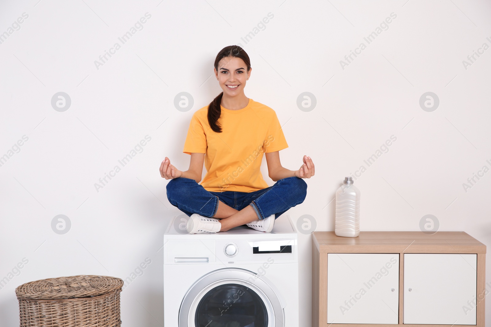 Photo of Young woman meditating on washing machine at home. Laundry day