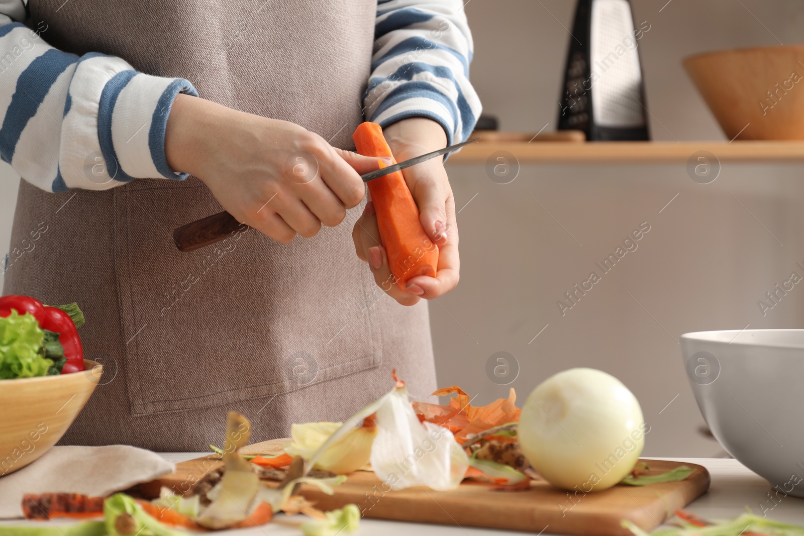 Photo of Woman peeling fresh carrot with knife at table in kitchen, closeup