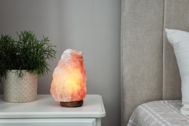 Photo of Beautiful Himalayan salt lamp and green houseplant on white table in bedroom, space for text