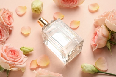 Photo of Bottle of perfume, beautiful roses and petals on beige background