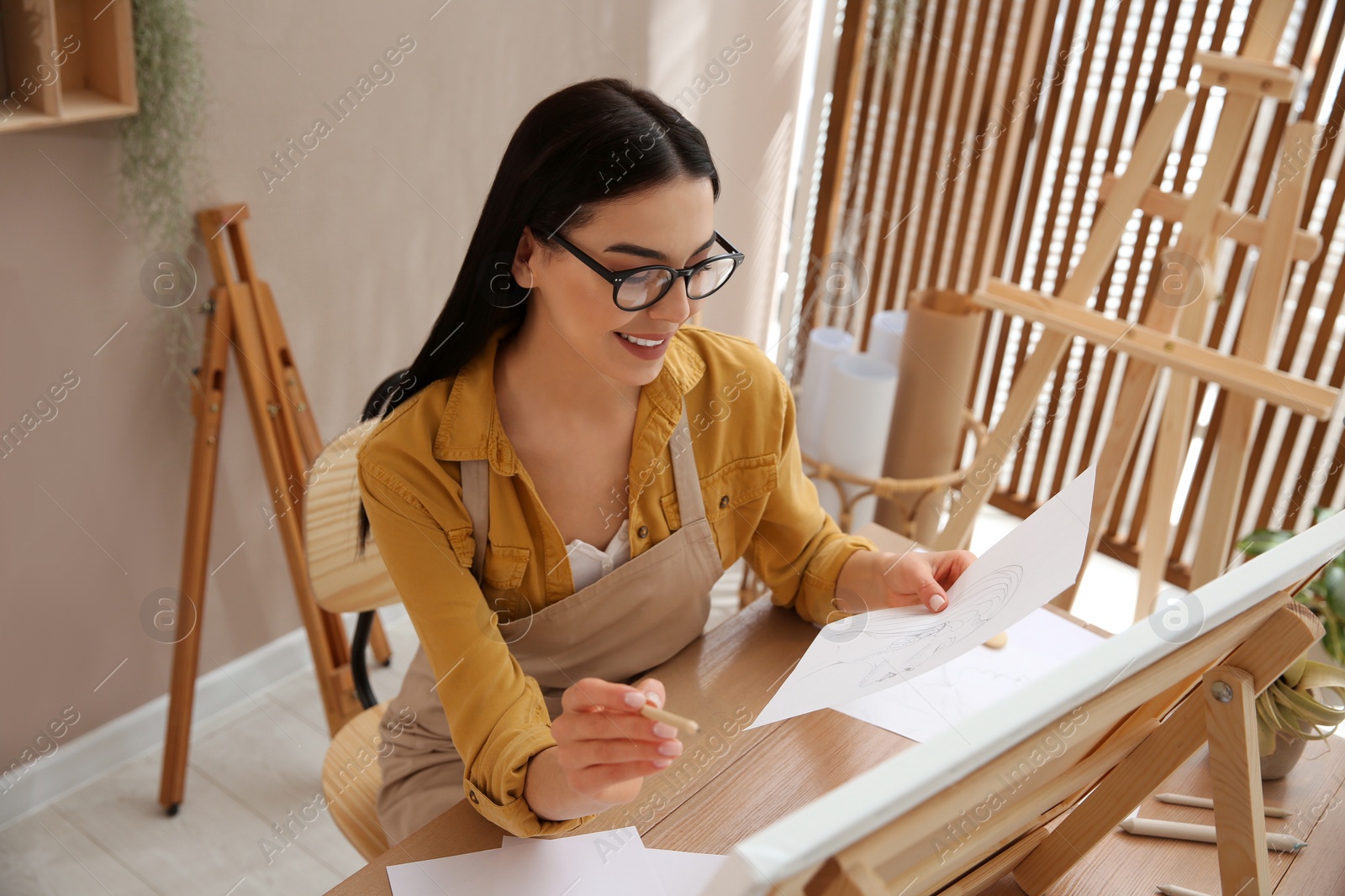 Photo of Young woman drawing on easel with pencil at table indoors