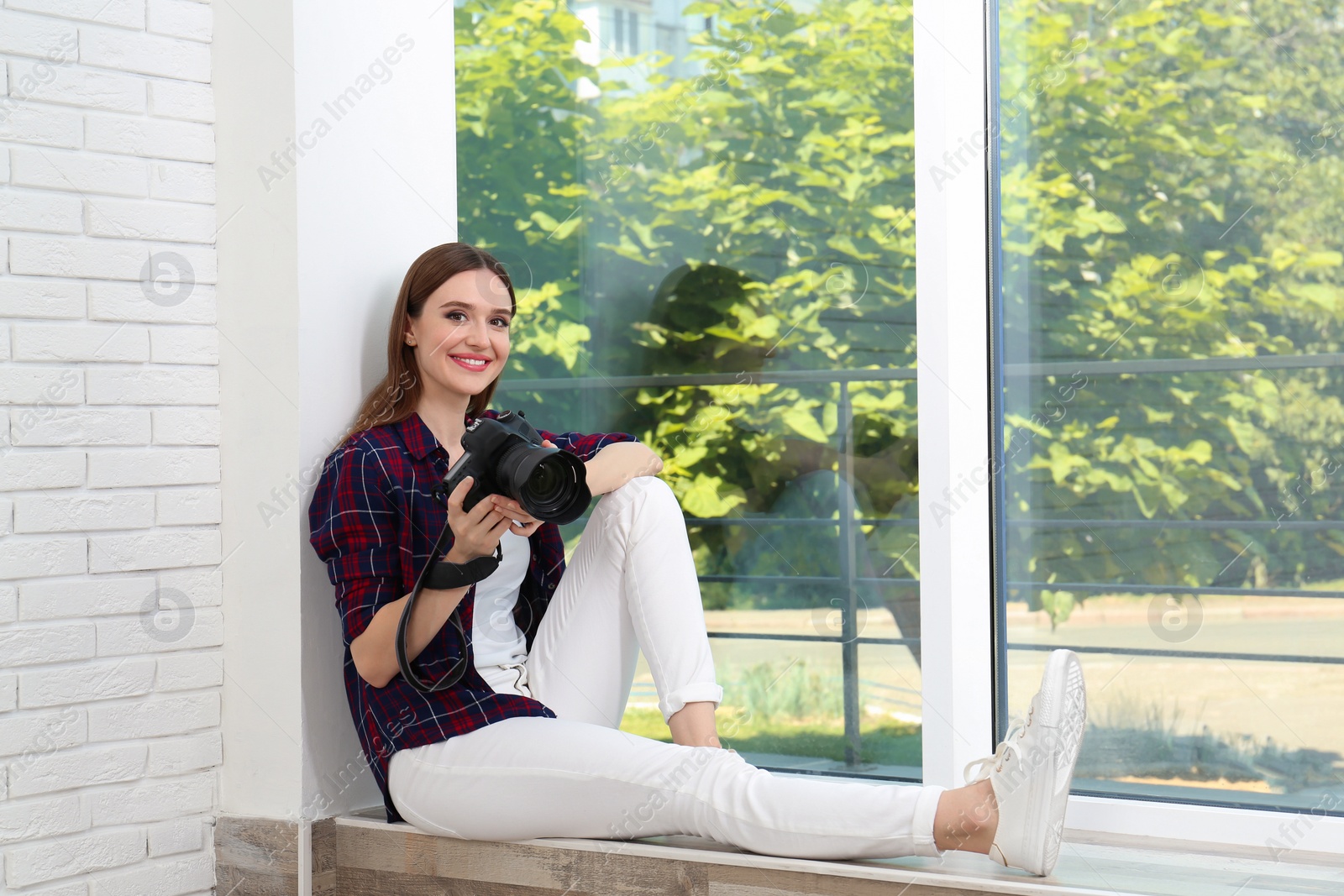 Photo of Professional photographer with modern camera sitting near window indoors