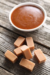 Photo of Yummy candies and caramel sauce in bowl on wooden table, closeup