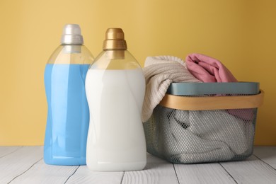 Photo of Bottles of fabric softener and clothes in basket on white wooden table