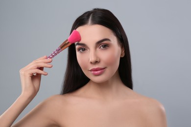 Woman applying makeup with brush on light grey background