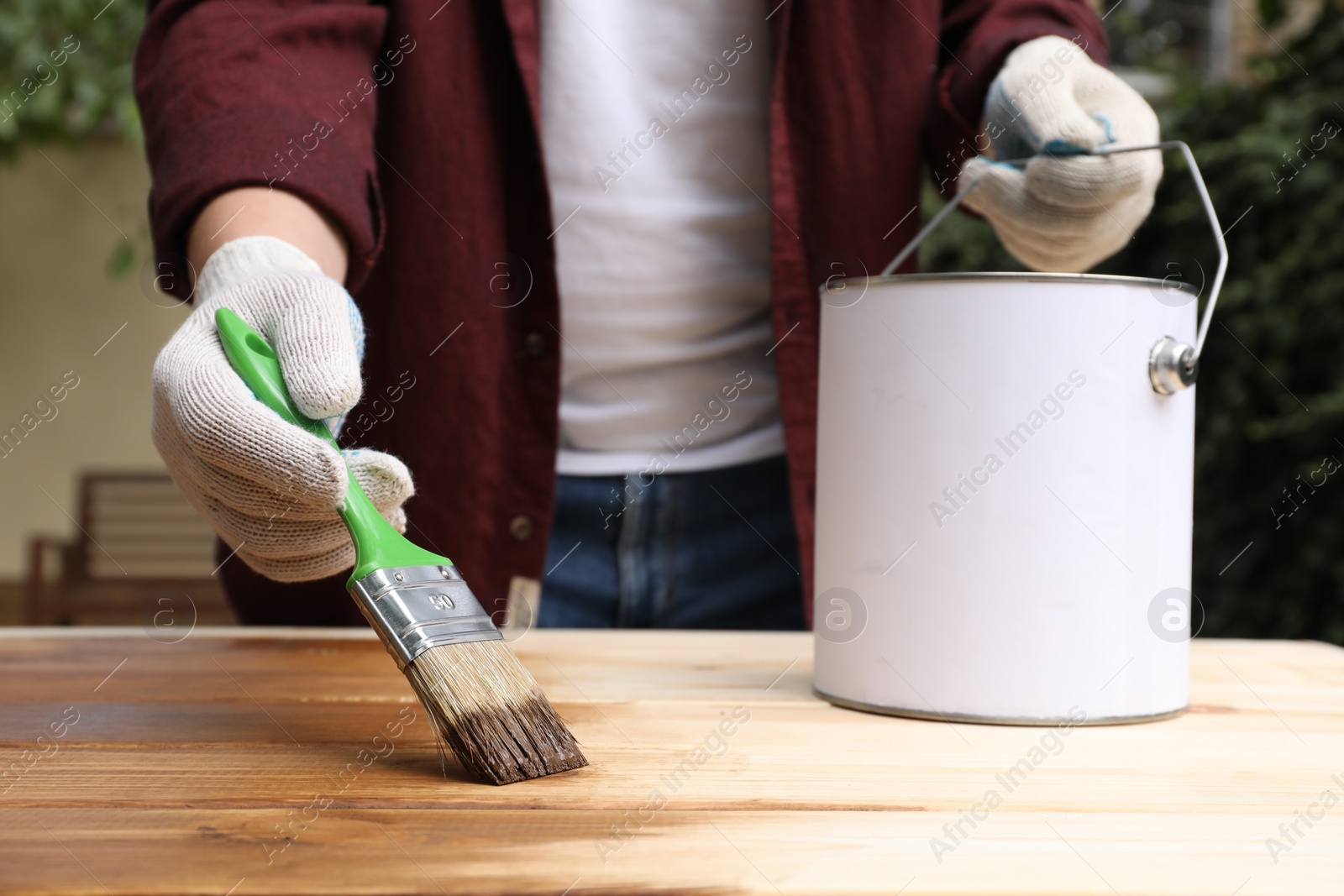 Photo of Man applying wood stain onto wooden surface outdoors, closeup