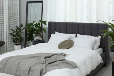 Large comfortable bed and beautiful houseplants in room. Bedroom interior