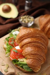 Photo of Tasty croissant with salmon, avocado, mozzarella and lettuce on table, closeup