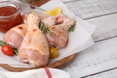 Photo of Marinade, raw chicken drumsticks, rosemary and tomatoes on white wooden table. Space for text