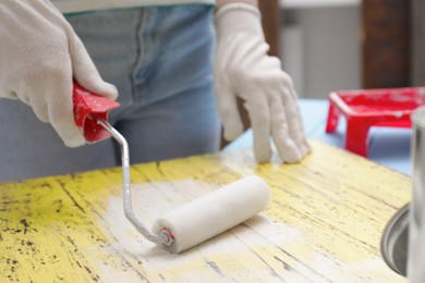 Photo of Woman using roller to paint plank with white dye indoors, closeup