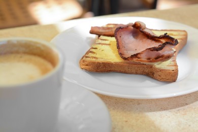 Delicious sandwich served with coffee for breakfast on beige table, closeup